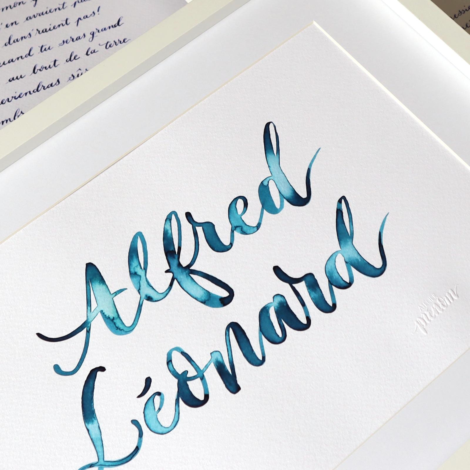 Le prénom Alfred Léonard calligraphié à l'aquarelle bleue, vu de près sur son passe-partout
